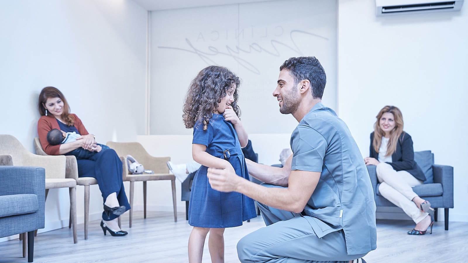 Doctor de la Clínica Nayef saludando a una niña en la sala de espera, en familia